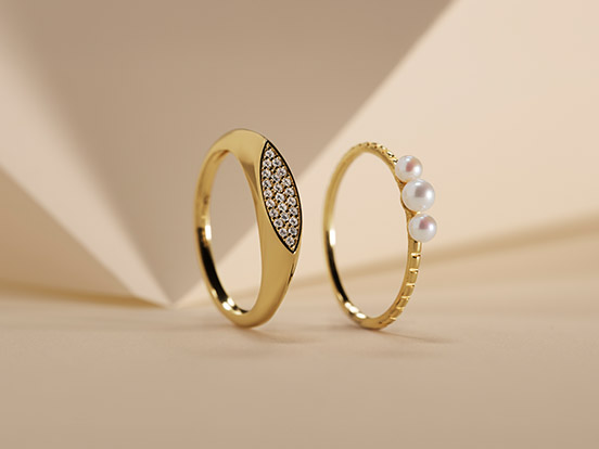 Link zu Ringen. Ein goldener Ring mit Farbsteinen und ein goldener Ring mit zwei Perlen.