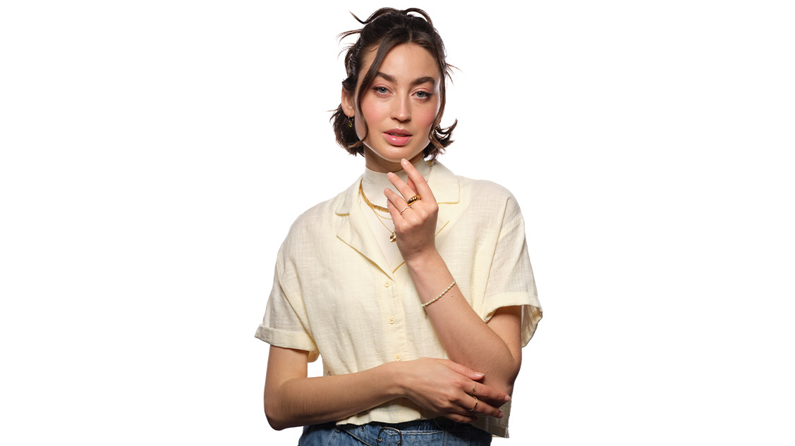 Jonge vrouw met crèmekleurige blouse draagt gouden sieraden - ringen, armbanden, kettingen en creolen
