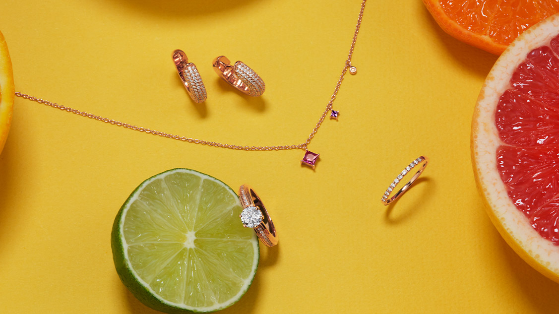Sieraden in roségoud op een gele achtergrond. Ketting, een paar oorbellen en twee ringen.