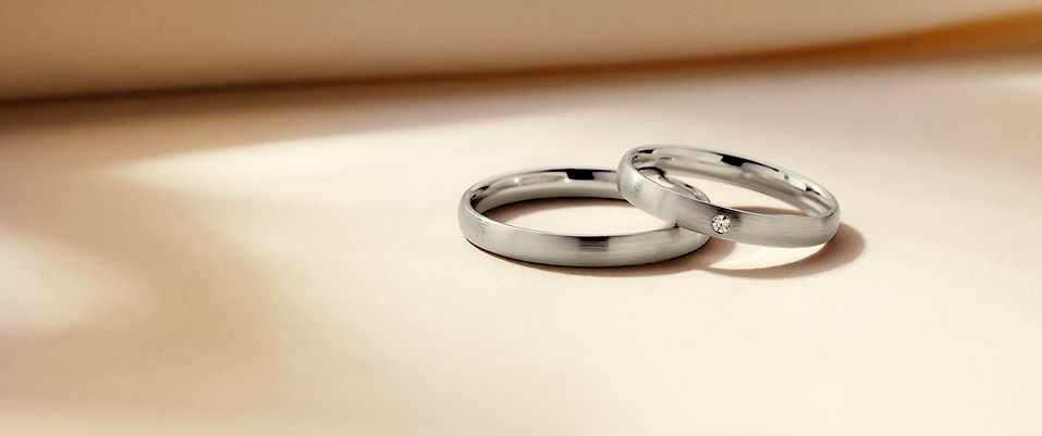 Zwei Trauringe auf hellbeigem Untergrund