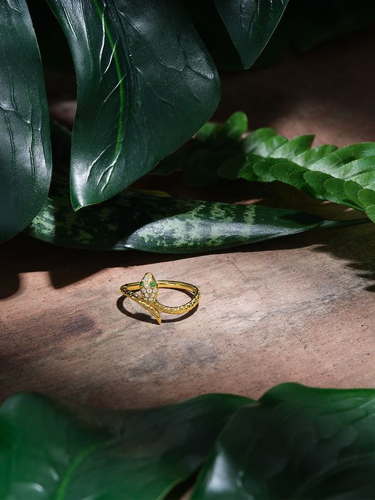 Goldener Guia Ring im Schlangen Design vor grünem Blätter Hintergrund.
