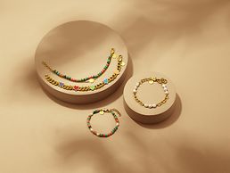 Drei goldfarbene Armbänder mit bunten Elementen und ein goldfarbenes Armband mit Perlen werden gemeinsam präsentiert.