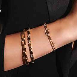 Goldarmbänder mit schwarzen und weißen Steinen an einem Arm von einer Frau.