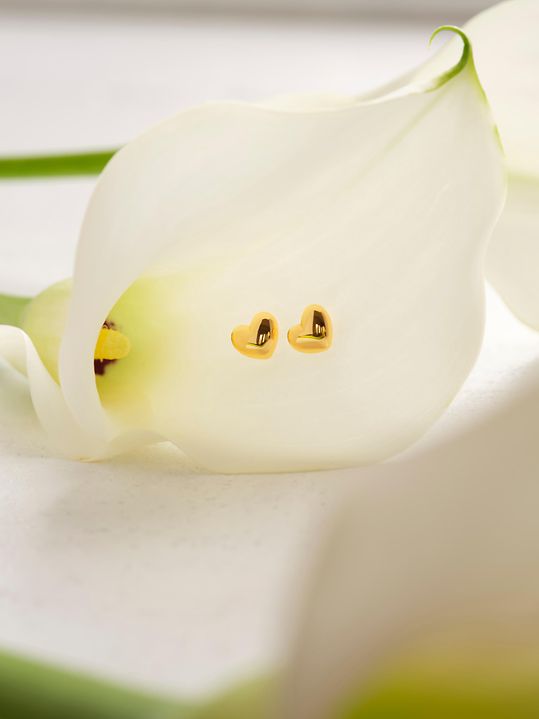 Herzförmige Ohrstecker dekorativ in einer weißen Blüte platziert.