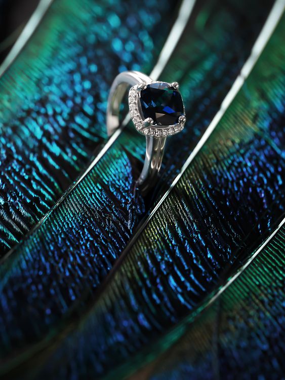 Ein großer blauer Farbsteinring zwischen grün-blauen Pfauenfedern.