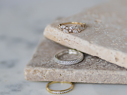Drei Ringe auf Steinplatten: zwei goldene mit Zirkonia, ein Silberner.