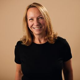 Brustkrebsbetroffene Steffi mit einem schwarzen T-shirt vor einem beigen Hintergrund.