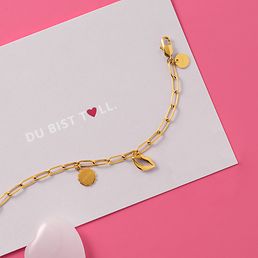 Ein goldenes GMK Armband mit Charms auf pinkem Hintergrund.