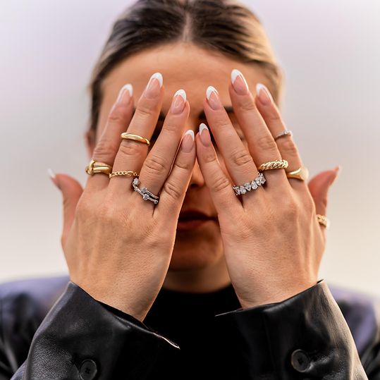 Zwei mit vielen Ringen geschmückte Frauenhände, die vor das Gesicht gehalten werden