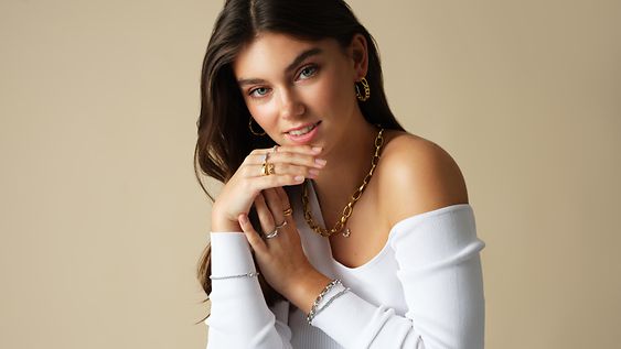 Eine Frau im weißen Off-Shoulder-Pullover mit vielen Ringen, Ketten und Ohrringen